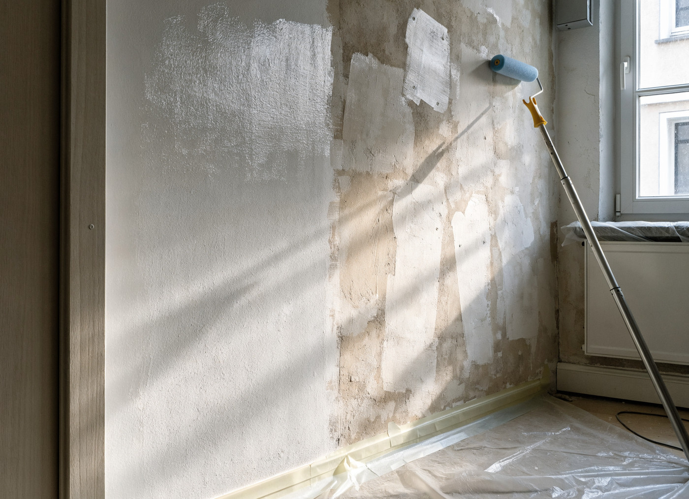 Frisch gespachtelte und weiß gestrichene Wand mit Farbroller und Abdeckfolie